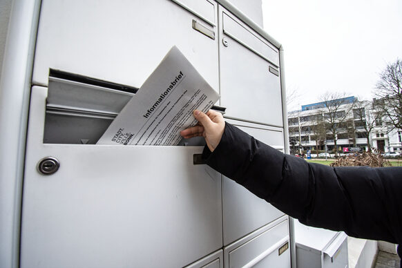 Ein Informationsbrief der Stadtverwaltung wird in einen Briefkasten gesteckt.