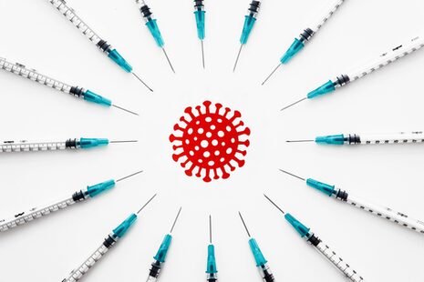 Fotomontage: Impfspritzen liegen im Kreis angeordnet um ein gezeichnetes Coronavirus