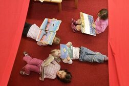 Kindergartenkinder liegen auf einem roten Teppich und schauen verschiedene Bilderbücher an