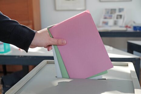 Eine Hand wirft farbige Stimmzettel in eine Wahlurne