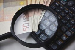 Blick durch eine Lupe auf 50-Euro-Scheine und einen Taschenrechner