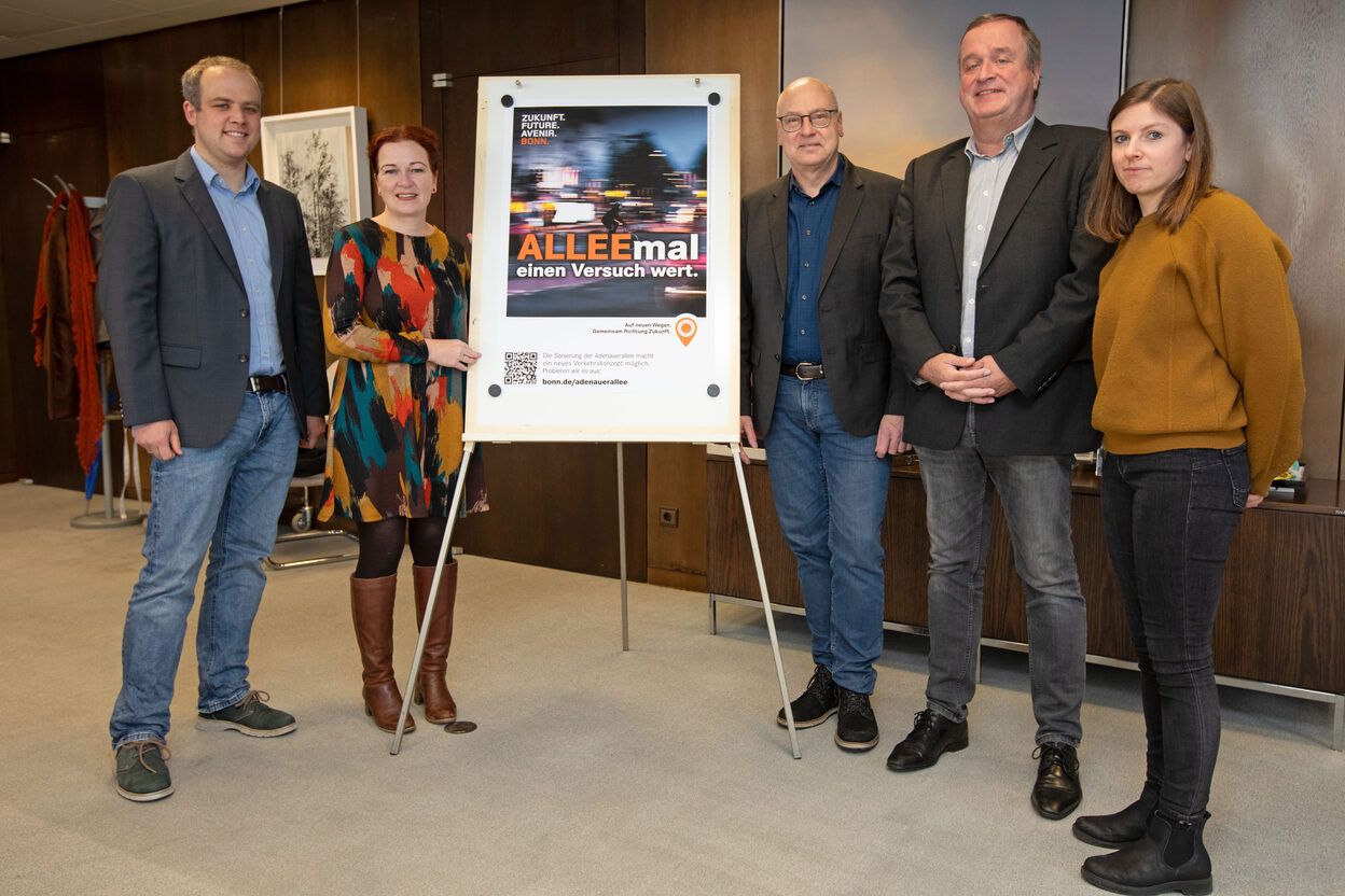 Vertreter*innen der Stadtverwaltung präsentieren mit Oberbürgermeisterin Katja Dörner ein Plakat, mit dem die Stadt auf den Dialog zur Adenauerallee aufmerksam machen wird.