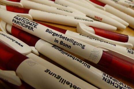 Viele Kugelschreiber mit dem Aufdruck Bürgerbeteiligung in Bonn liegen auf einem Tisch