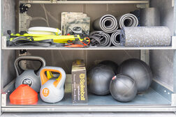 Das Bild zeigt den Inhalt einer Sportbox: Gewichte, Medizinbälle, Yogamatten und auch Fresbees.