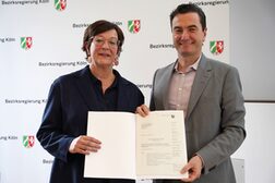 Das Bild zeigt links Petra Denny, Leiterin des Stadtplanungsamtes der Stadt Bonn, und rechts Regierungspräsident Dr. Thomas Wilk bei der ÜBergabe des Zuwendungsbescheids für die Städtbauförderung NRW.