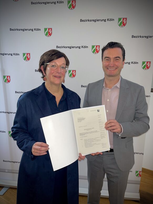 Das Bild zeigt links Petra Denny, Leiterin des Stadtplanungsamtes der Stadt Bonn, und rechts Regierungspräsident Dr. Thomas Wilk bei der Übergabe des Zuwendungsbescheids für die Städtebauförderung NRW.