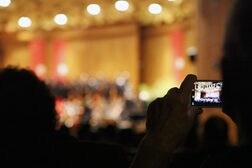 Ein Zuhörer fotografiert mit einem Smartphone ins Publikum hinein