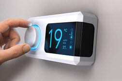 Eine Hand dreht an einem Hausthermostat die Temperatur auf 19 Grad herunter