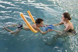 Kind mit Schwimmnudel beim Schwimmunterricht