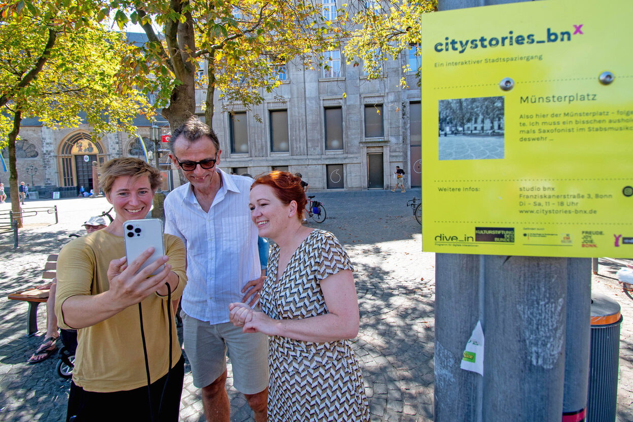 Oberbürgermeisterin Katja Dörner lässt sich von Videokünstlerin Annika Ley und dem Leiter des Fringe-Ensembles, Frank Heuel, die neue App "City Stories Bonn" vorführen.