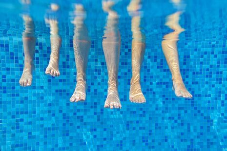 Unterwasseraufnahme von sechs Beinen, die im Wasser hängen