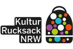 Das Bild zeigt einen schwarzen Rucksack mit bunten Punkten. Daneben steht „Kulturrucksack NRW“.