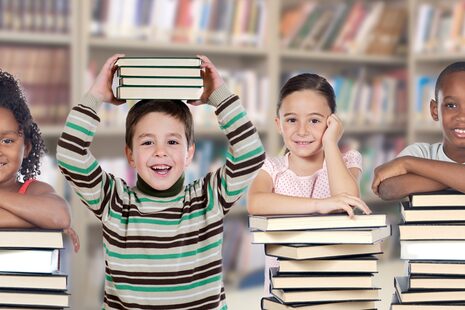 Vier Kinder mit Bücherstapeln vor sich in einer Bibliothek