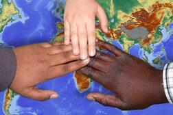 Hände in verschiedenen Hauttönen liegen übereinander auf einer Weltkarte.