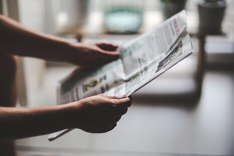 Eine Person liest stehend in einer Tageszeitung