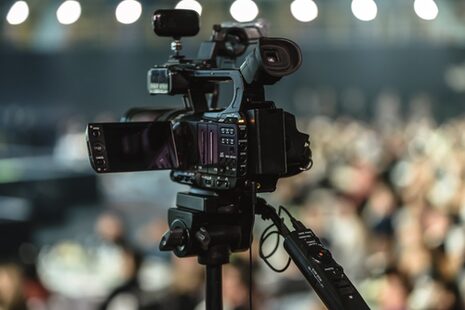 Eine Videokamera vor einem undeutlich zu erahnenden Publikum
