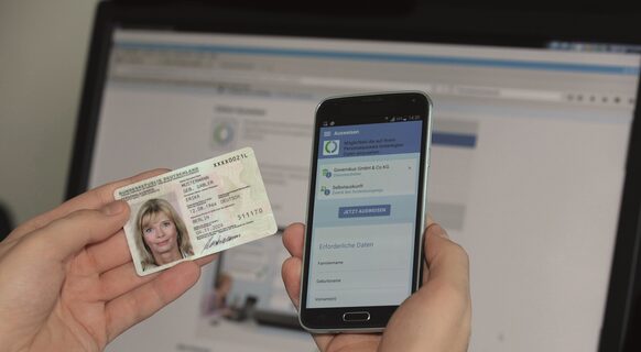 Ein Person hält einen neuen Personalausweis mit elektronischer Identifikation neben ein Smartphone mit geöffneter App