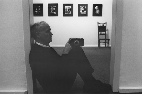 Franz Fischer sitzt in einem Türrahmen mit einer Kamera auf seinen Knien