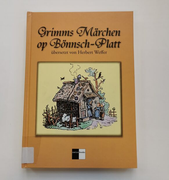 Buch "Grimms Märchen op Bönnsch-Platt" übersetzt von Herbert Weffer, beige-gelbes Buchcover mit Hexenhaus als Motiv.