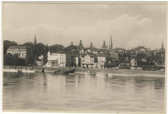 Das Schwarz-Weiß-Bild zeigt das Rheinufer in Bonn mit kleinen Ausflugsschiffen.
