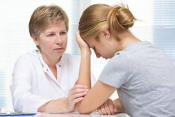 Frau im Gespräch mit einer Ärztin beziehungsweise Therapeutin. Die Patienten fasst sich verzweifelt an den Kopf.