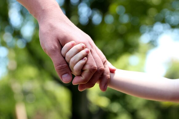 Die Hand eines Kindes vertrauensvoll in die Hand eines erwachsenen Mannes gelegt