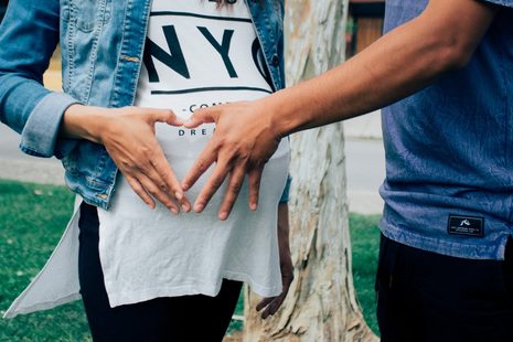 Eine schwangere Frau und ein Mann halten ihre Hände in Herzform vor den Babybauch.