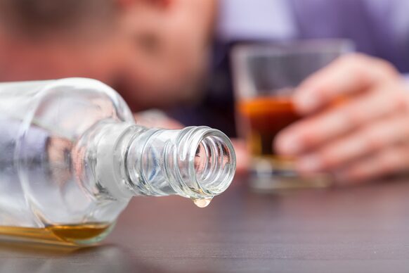 Fast leere Alkoholflasche mit betrunkenem Mann im Hintergrund
