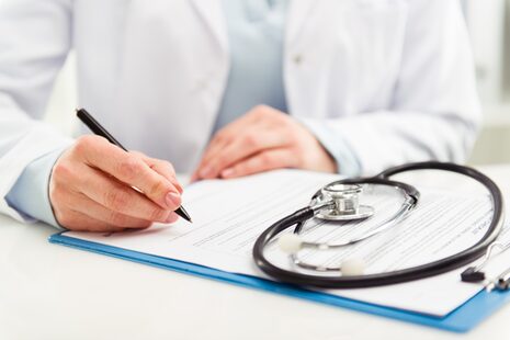 Ein Arzt macht sich Notizen, auf dem Schreibtisch liegt ein Stethoskop
