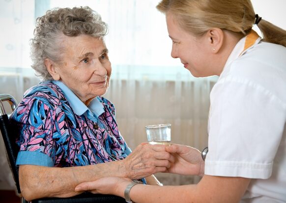 Altenpflegerin reicht einer Seniorin ein Glas Wasser