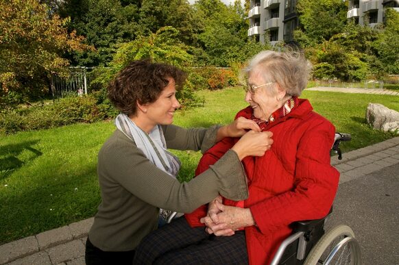 Spaziergang einer Pflegerin mit einer Seniorin im Rollstuhl