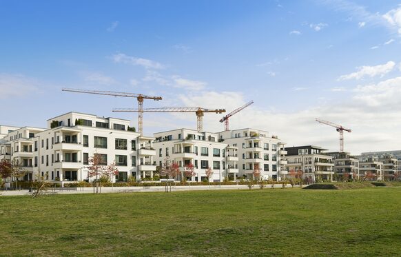 Neu gebaute Apartmenthäuser mit Kränen und Wiese im Vordergrund.