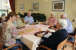 Senior*innen sitzen mit einer Betreuerin um einen Tisch und spielen Bingo.