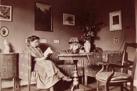 Schwarz-weiß Foto von Elly Heuss-Knapp, mit einem Buch auf einem Sofa sitzend