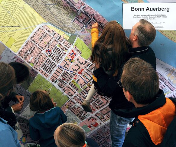 Kinder und ein Erwachsener betrachten eine Plankarte von Bonn Auerberg