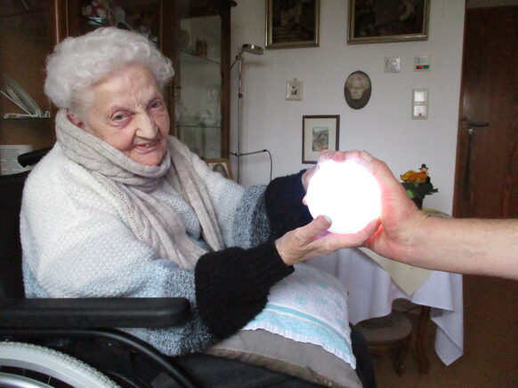 Eine alte Dame im Rollstuhl hält einen leuchtenden Ball in den Händen.