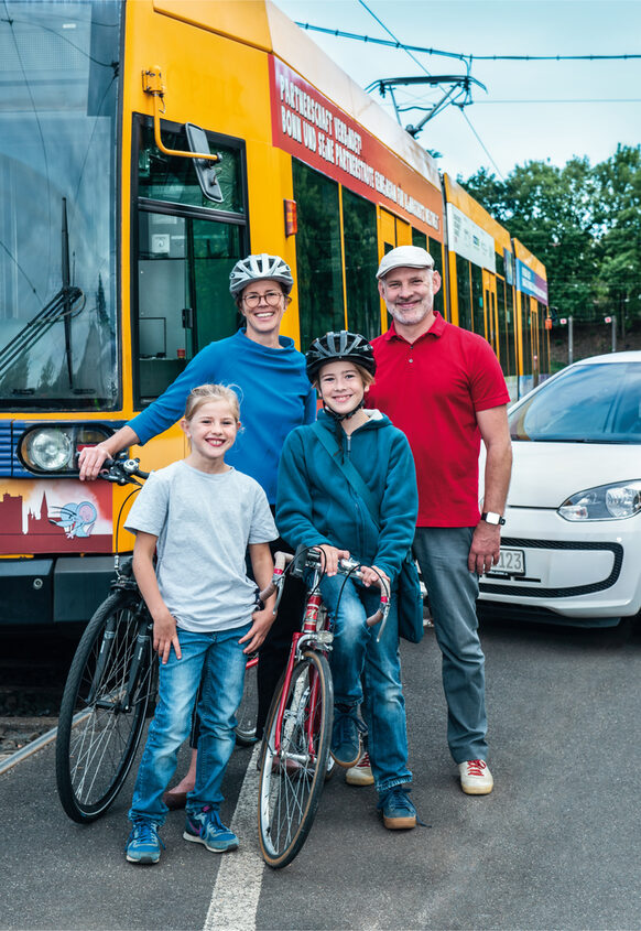Familie mit Fahrrädern steht vor einem Bus und einem Pkw.