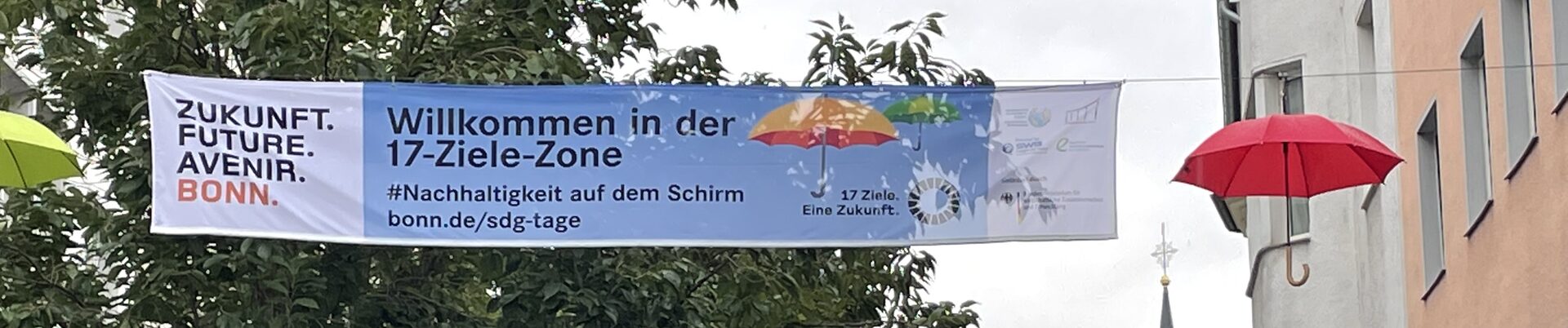 Banner "17-Ziele-Zone" zu den SDGs in der Friedrichstraße, die  mit bunten Regenschirmen geschmückt ist.