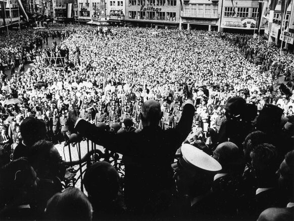 Charles de Gaulle steht auf der Rathaustreppe und spricht zu der auf dem Markt versammelten Menschenmenge