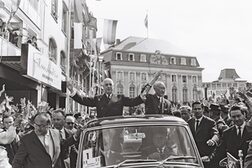 Der französische Präsident Charles de Gaulle und Bundeskanzler Konrad Adenauer fahren 1962 in einem offenen Auto über den Bonner Markt und winken