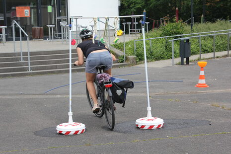 Eine Frau fährt mit dem Fahrrad unter einem Hindernis durch.