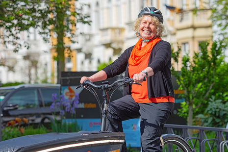 Eine lächelnde Frau fährt auf einem Lastenrad, das Sie an einer Mobilstation in Bonn ausleihen kann.