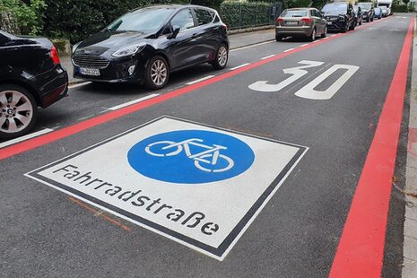 Das Bild zeigt die neue Markierung einer Fahrradstraße in Bonn mit roten Streifen am Fahrbahnrand..