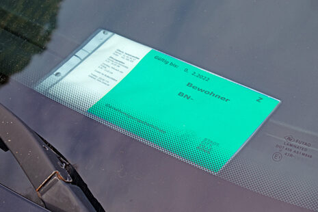 Das Bild zeigt einen blauen Bewohnerparkausweis, der hinter der Windschutzscheibe eines Autos liegt
