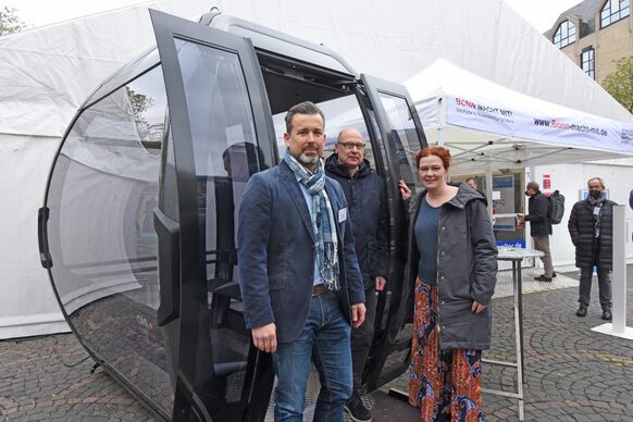 Oberbürgermeisterin Katja Dörner, Baudezernent Helmut Wiesner und Projektleiter Dirk Delpho (links) an der Seilbahnkabine vor dem Zelt der Infomesse auf dem Münsterplatz