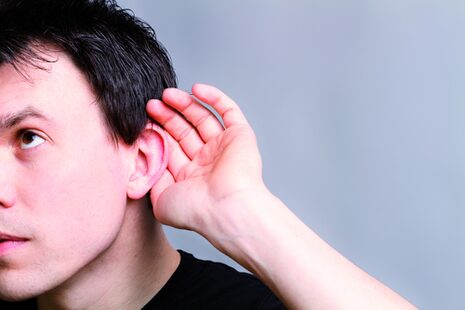 Ein schwerhöriger Mann hält sich die Hand hinter die Ohrmuschel, um besser hören zu können