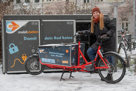 Das Bild zeigt eine Frau mit einem gemieteten Lastenrad vor einer Mobilstation in Bonn.