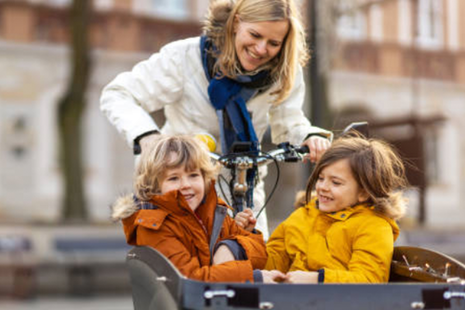 Eine Mutter fährt mit ihren beiden Kindern im Lastenrad durch die Stadt.
