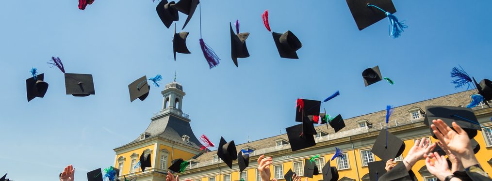 Uni-Absolventen werfen vor dem Uni-Hauptgebäude ihre Hüte in die Luft.