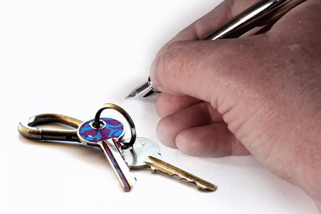 EIne Hand mit einem Füller zur Unterschrift, daneben liegt ein Schlüsselbund